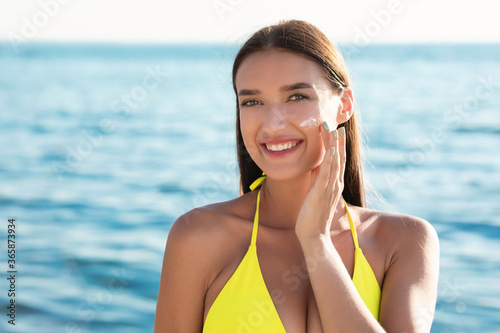 Tanned Woman Applying Suntan Lotion On Face Standing Near Sea © Prostock-studio