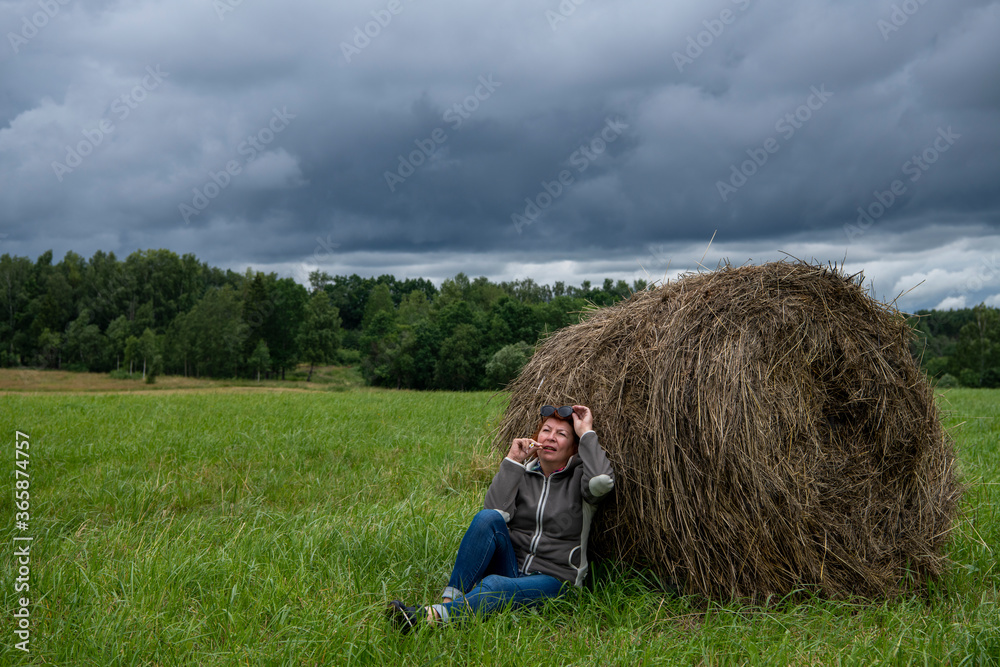 woman resting near a haystack in nature against a gray sky woman resting near a haystack in nature against a gray sky