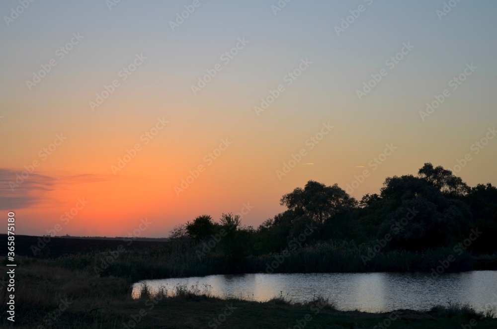 Natural silhouetted landscape. Sunset sky and two flying planes over the pond in the right.