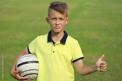 boy football player in a yellow t-shirt holds the ball in his hand. second hand shows thumbs up photo