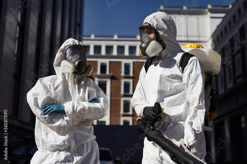 two professional disinfectors with disinfectant in the streets. professional workers in white protective wearing and gloves clean the area