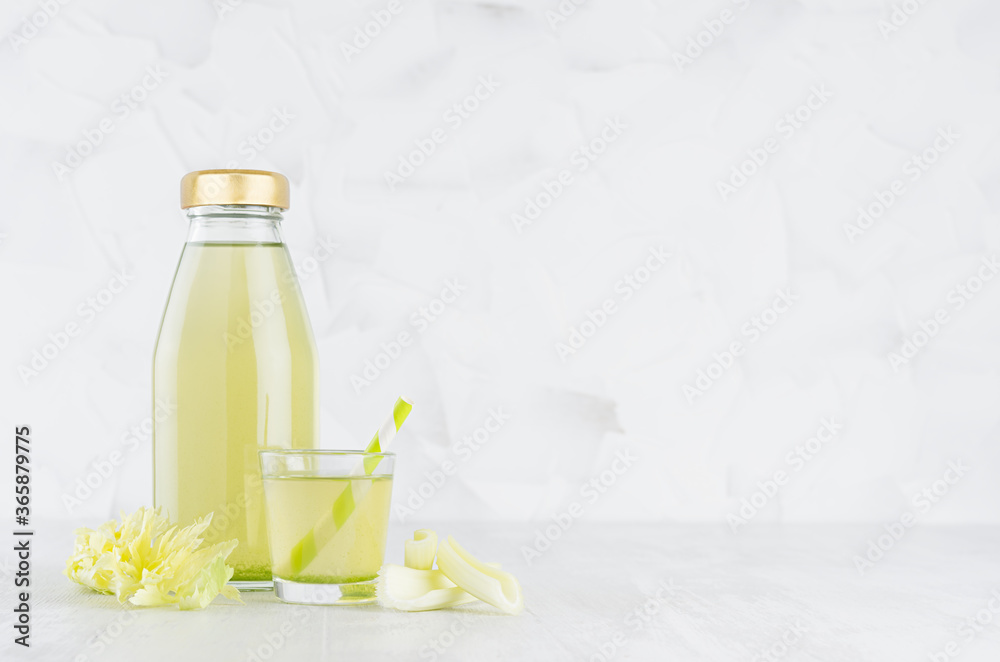 Fresh vegetable green celery juice in glass bottle mock up with glass, straw, stems in soft light white interior on wood table. Fresh vegetable green celery juice in glass bottle mock up with glass, straw, stems in soft light white interior on wood table.