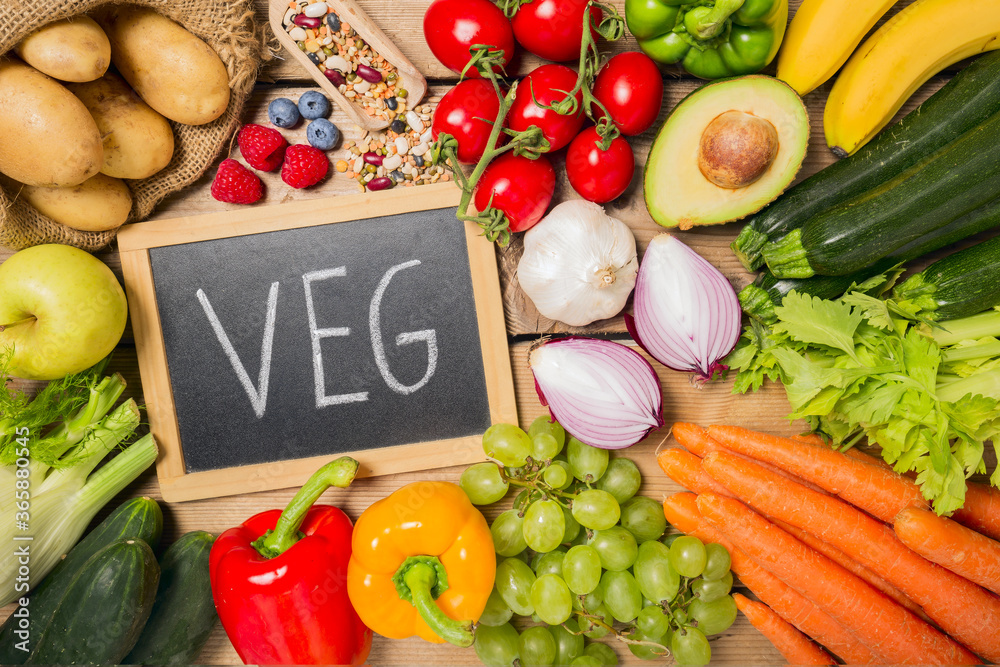 Black Chalk Board with VegTexts with Assorted Organic Veggies on Sides on Top of Wooden Table Black Chalk Board with VegTexts with Assorted Organic Veggies on Sides on Top of Wooden Table