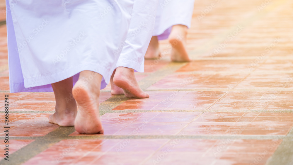 Female Bhuddism in white clothes walking slowly, meditation tranquil walk, without shoes in the temple.
