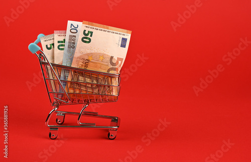 Euro banknotes in shopping cart over red