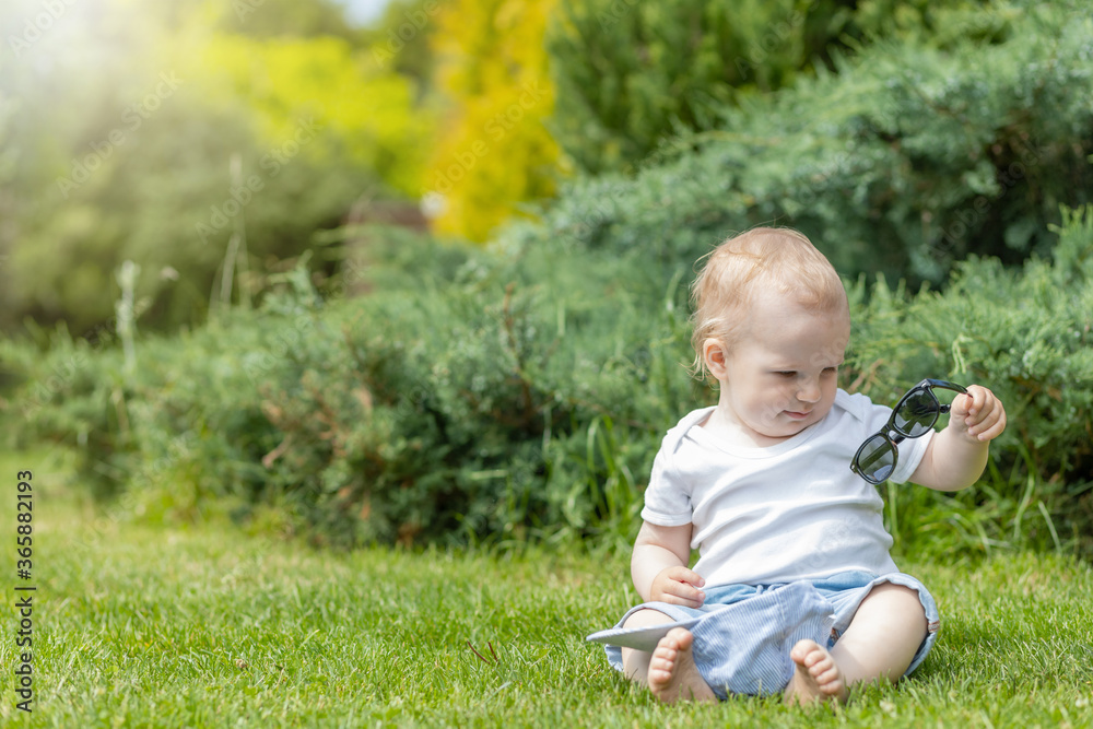 Little boy is viewing his sunglasses sitting in the garden Little boy is viewing his sunglasses sitting in the garden