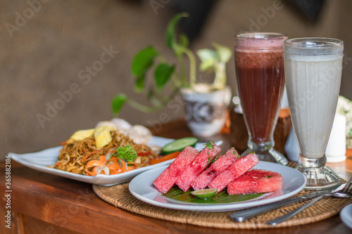 Balinese lunch served on a table with noodles, watermelon and colourful beverages decoration