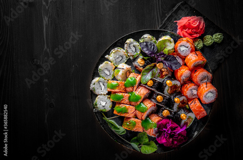 set of sushi roll with salmon, avocado, cream cheese, cucumber, rice, caviar, eel, tuna in plate on black wooden table background