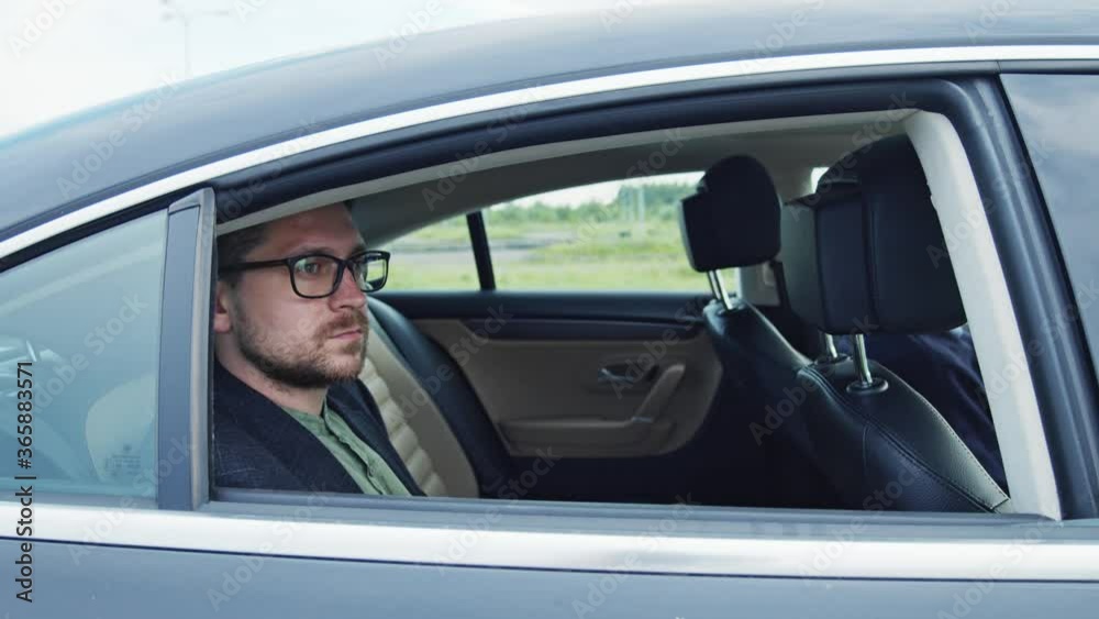Young thoughtful businessman sitting on back seat of car heading to the office with personal driver. Business people. Passenger. Transport. Young thoughtful businessman sitting on back seat of car heading to the office with personal driver. Business people. Passenger. Transport.