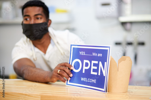 cafe worker open cafe to get orders, he is ready to serve clients, wearing black protective mask photo