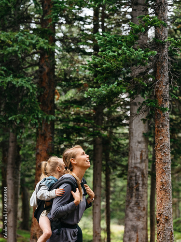 Mom carrying daughter on her back through the woods while hiking in Colorado
