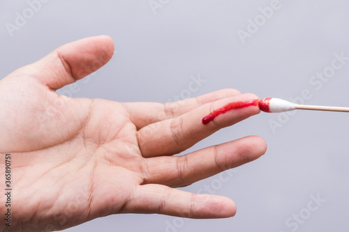 Use a cotton swab to wipe the blood at the wound on fingertips that are bleeding on white background.