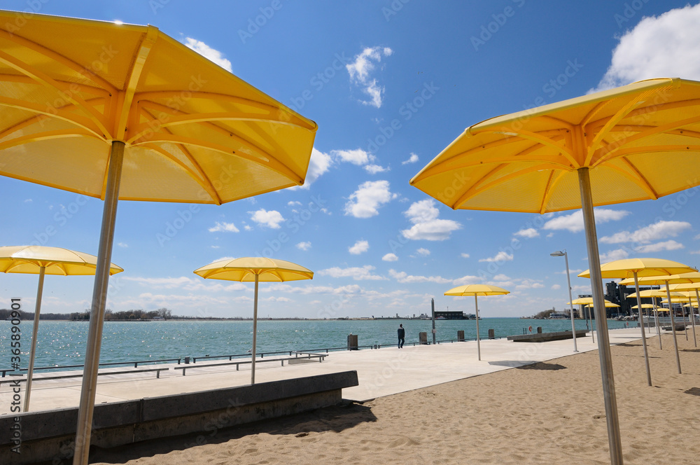 Yellow metal beach umbrellas at urban beach of HTO Park on Lake Ontario with Toronto Island airport