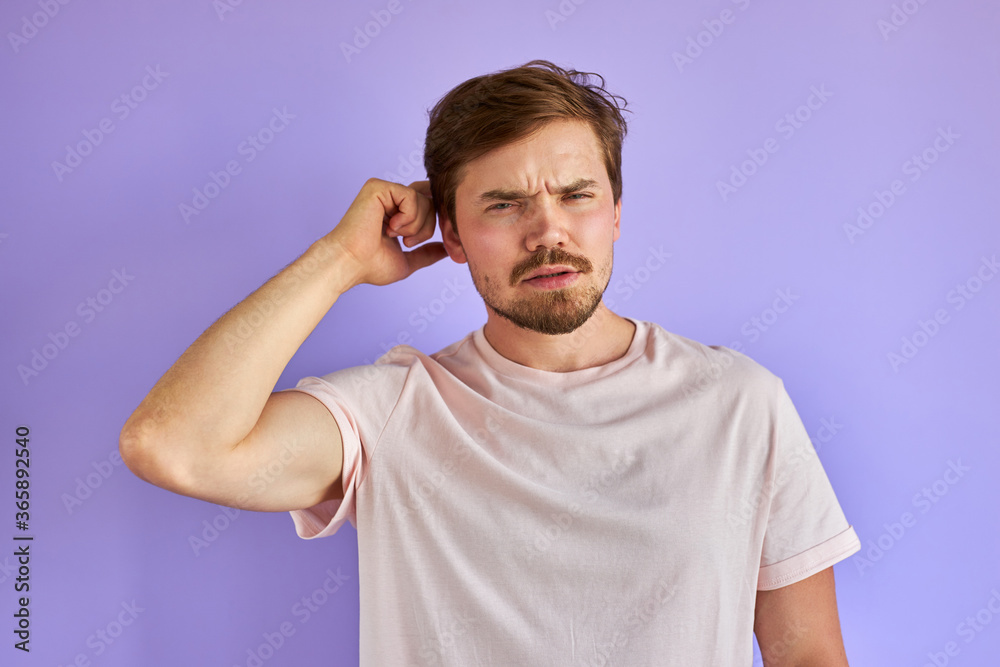 young preplexed man with thoughtful or disgusted expression, isolated on purple background. people sincere emotions lifestyle concept. young preplexed man with thoughtful or disgusted expression, isolated on purple background. people sincere emotions lifestyle concept.