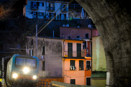 A night train's headlights shine as it enters a tunnel in the evening at Vernazza Italy, on the Cinque Terre coast with the hillside town behind photo