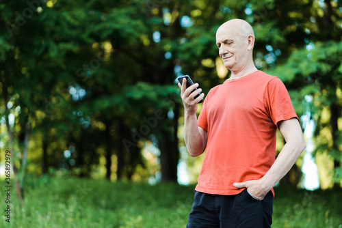 Portrait of a senior man standing with a phone in his hands in the park. High quality photo