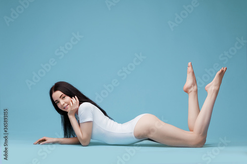 Beautiful slim woman posing in white bodysuit. Fit and sexy female in underwear swimsuit. Blue background. Free space for text.