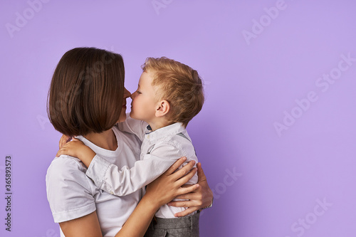 portrait of affectionate mother and son isolated over purple background. cute mother hugs her child, going to kiss photo