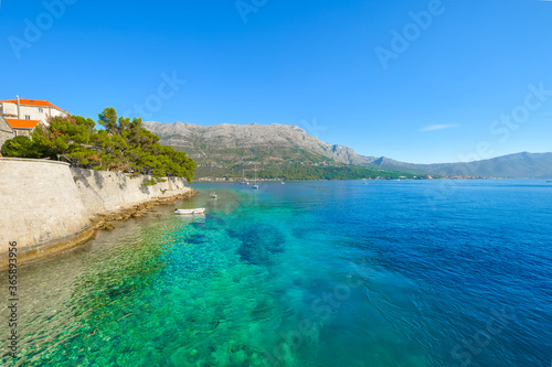Fototapeta Naklejka Na Ścianę i Meble -  A small white boat and medieval wall along the blue green sea coast near Hvar and Dubrovnik, Croatia on the Dalmation Coast