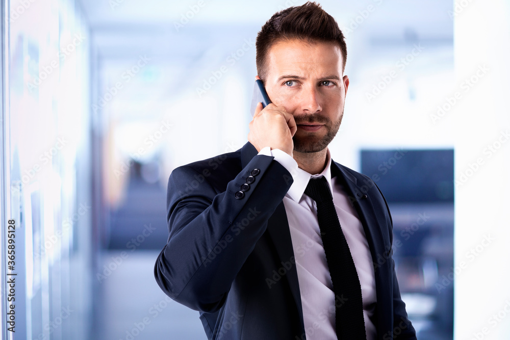 Thinking businessman standing in the office while having business call Thinking businessman standing in the office while having business call