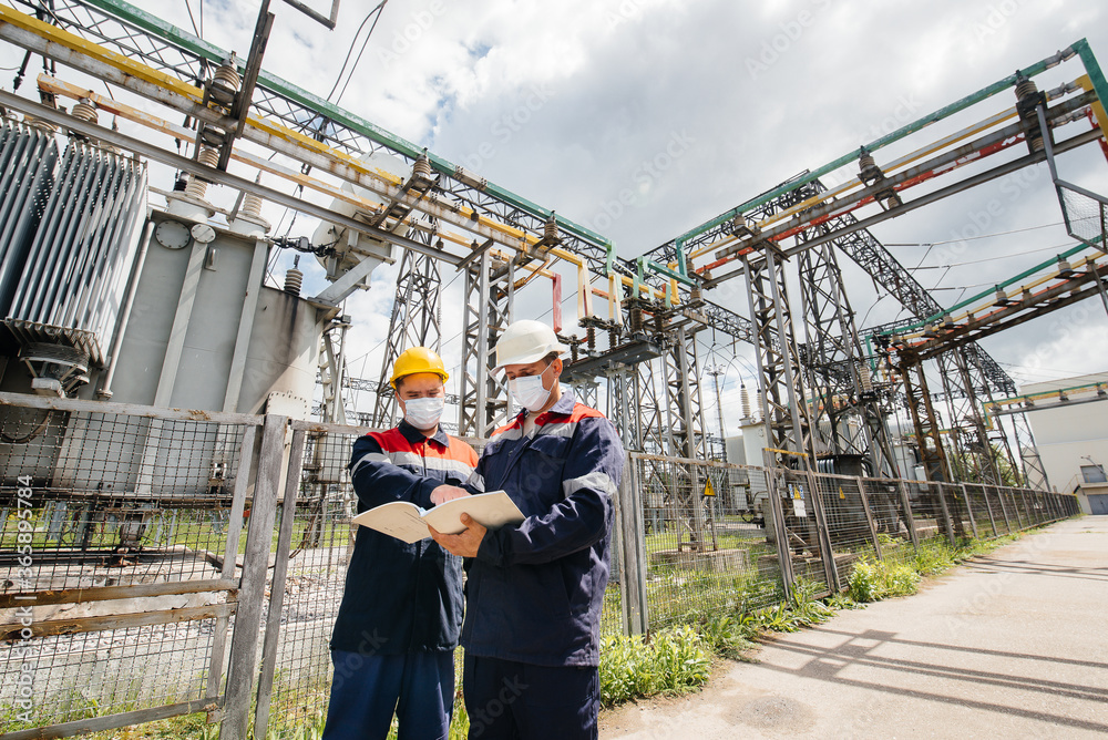 Engineers electrical substations conduct a survey of modern high-voltage equipment in the mask at the time of pandemia. Energy. Industry