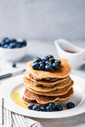 Stack of pancakes with blueberries and maple syrup on white plate, vertical orientation, copy space for text
