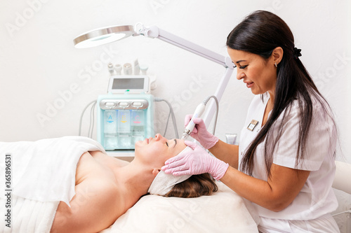 Beauty salon. A cosmetologist in rubber gloves does a aqua peeling procedure on the face. In the background, a cosmetology device. Concept of professional cosmetology and beauty