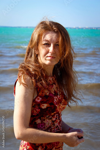 A serious young woman on the beach with gorgeous red hair and freckles. © buena17