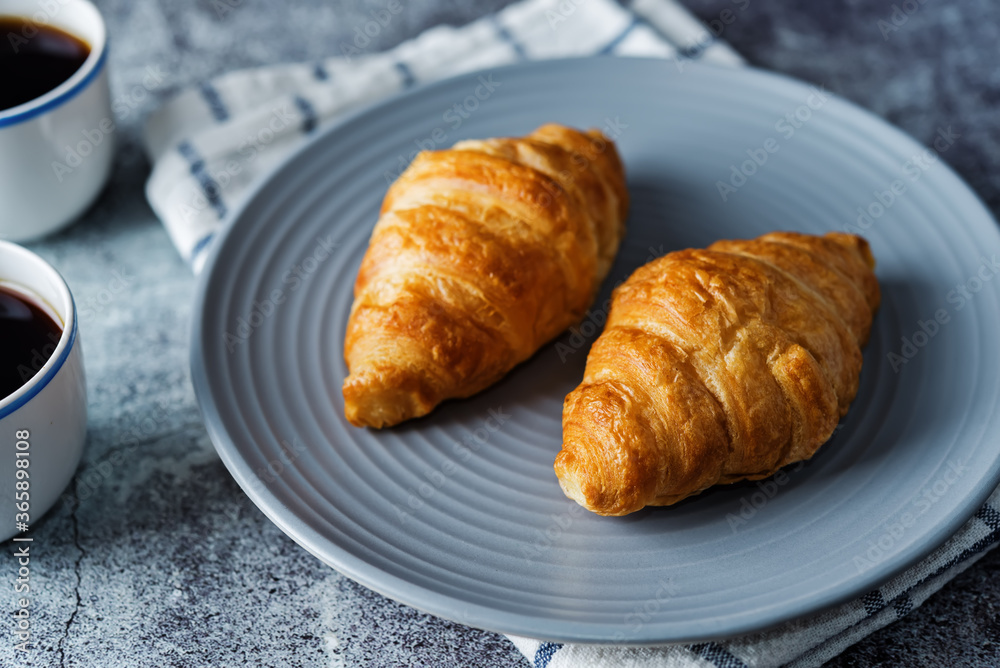 Fresh croissants on a plate with cups of coffee