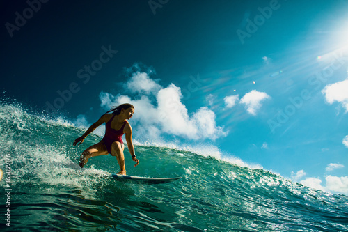 Fototapeta Professional Surfer Girl riding wave on surfing board under bright sun on background