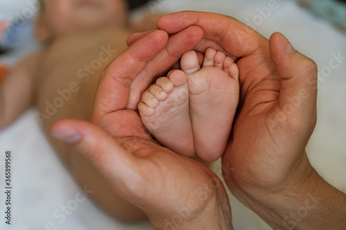 Little feet of the kid in the male hands of the dad