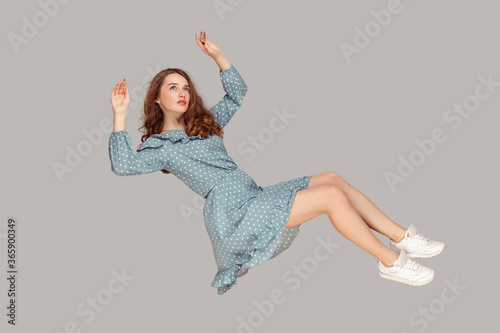 Hovering in air. Full length beautiful pensive girl in vintage ruffle dress levitating flying in mid-air, looking up with dreamy relaxed expression. indoor studio shot isolated on gray background