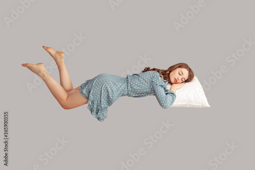 Relaxed girl in vintage ruffle dress levitating in mid-air, sleeping on stomach lying comfortable cozy on pillow, keeping eyes closed, watching peaceful dream. indoor studio shot isolated on gray photo