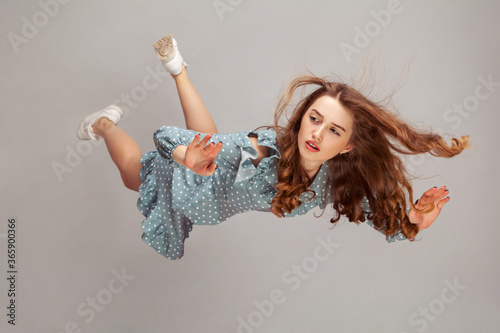 Beautiful girl levitating in mid-air, falling down and her hair messed up soaring from wind, model flying hovering with dreamy peaceful expression. indoor studio shot isolated on gray background photo