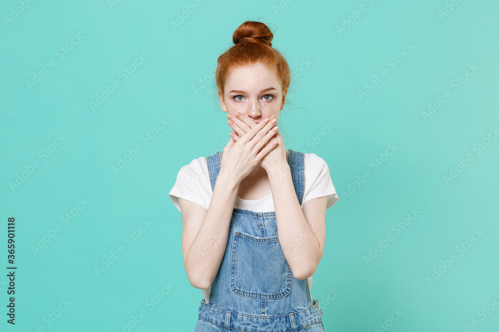 Young readhead girl in casual denim clothes posing isolated on blue turquoise wall background studio portrait. People sincere emotions lifestyle concept. Mock up copy space. Covering mouth with hands. Young readhead girl in casual denim clothes posing isolated on blue turquoise wall background studio portrait. People sincere emotions lifestyle concept. Mock up copy space. Covering mouth with hands.