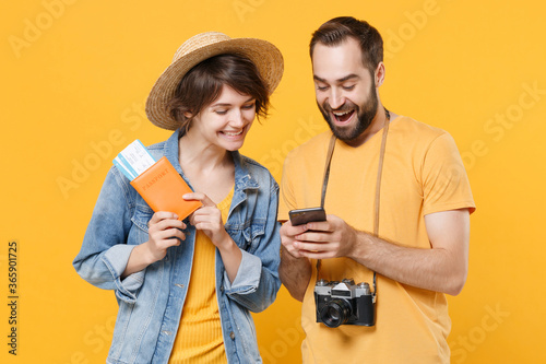 Funny tourists couple friends guy girl in summer clothes isolated on yellow background. Passenger traveling abroad on weekends. Air flight journey concept. Hold passport tickets using mobile phone.