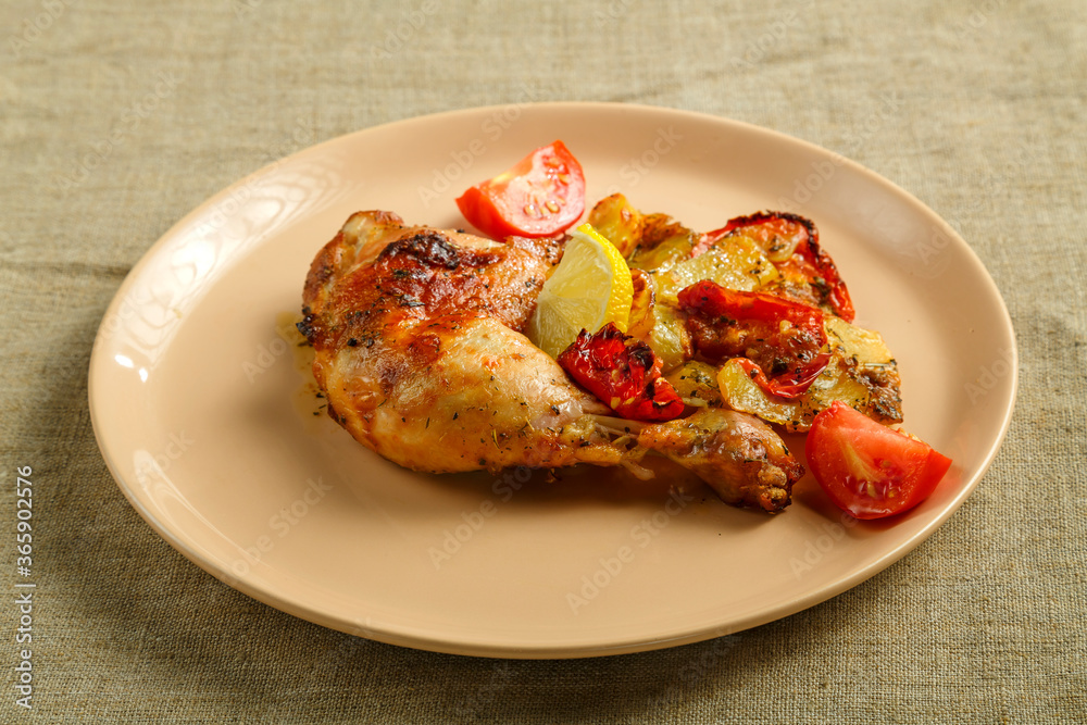 Baked chicken leg with potatoes and tomato on a beige plate on a linen tablecloth.
