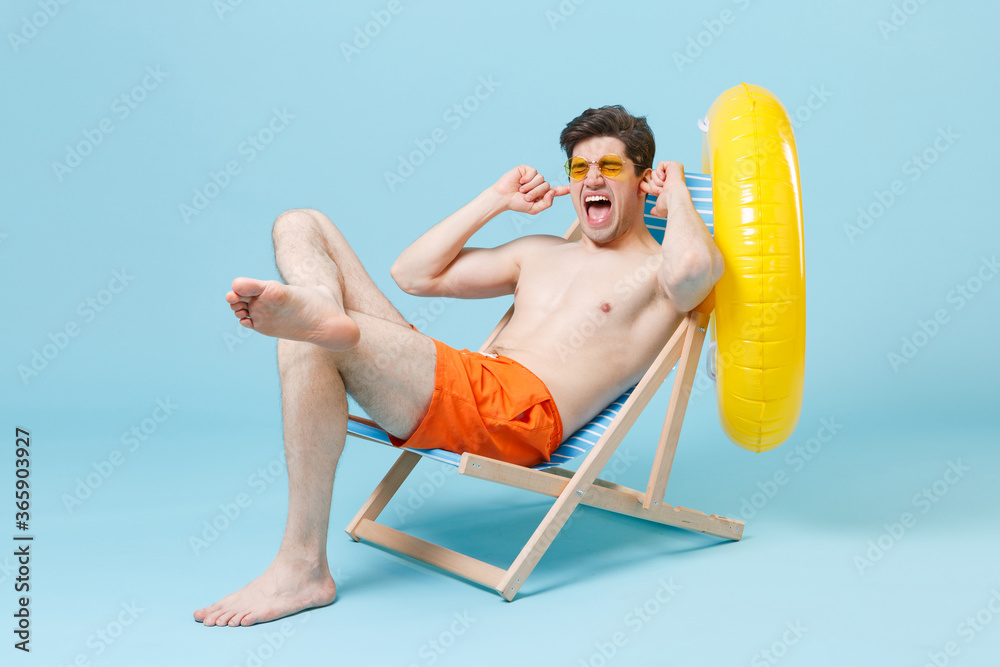 Crazy young man guy in orange shorts glasses sit on deck chair isolated