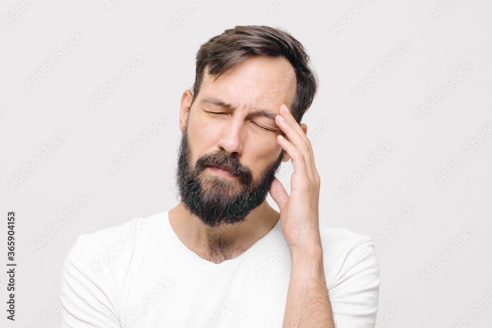 Close-up of young man in white casual t-shirt touching temples with fingers as if suffering from severe headache Close-up of young man in white casual t-shirt touching temples with fingers as if suffering from severe headache