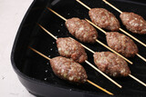 Kofta shashlik on wooden skewers is cooked in a grill pan, Closeup
