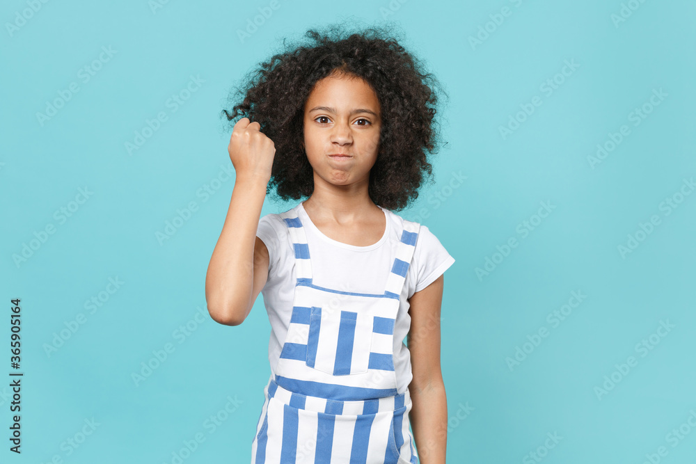 Dissatisfied little african american kid girl 12-13 years old in striped clothes isolated on pastel blue background studio portrait. Childhood lifestyle concept. Mock up copy space. Clenching fist. Dissatisfied little african american kid girl 12-13 years old in striped clothes isolated on pastel blue background studio portrait. Childhood lifestyle concept. Mock up copy space. Clenching fist.