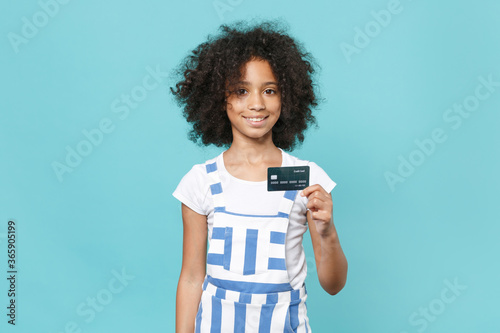 Smiling little african american kid girl 12-13 years old in striped clothes isolated on pastel blue background studio portrait. Childhood lifestyle concept. Mock up copy space. Hold credit bank card.