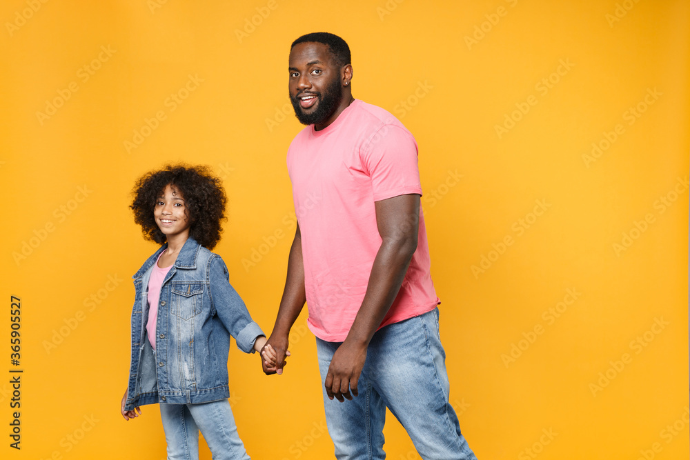 Obraz premium Smiling african american guy girl brother sister in denim pink clothes isolated on yellow wall background studio portrait. People lifestyle concept. Mock up copy space. Holding hands, walking going.