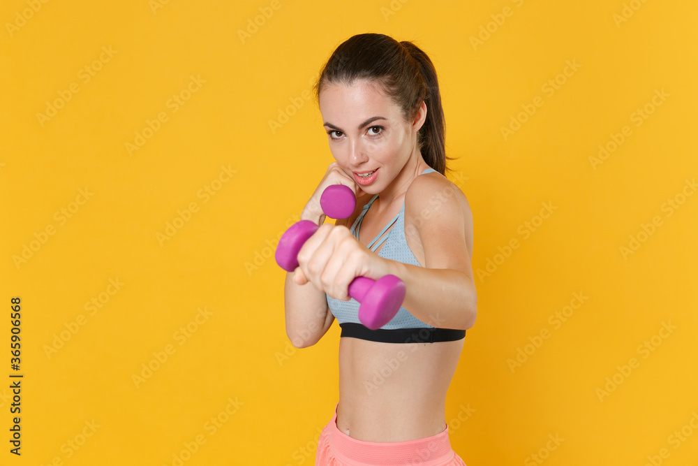 Strong young fitness sporty woman girl in sportswear working out isolated on yellow background studio. Workout sport motivation lifestyle concept. Mock up copy space. Doing exercise with dumbbells.