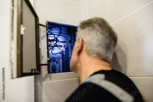 Aged plumber, repairman in uniform examining, inspecting pipes using flashlight in the bathroom. Repair service concept