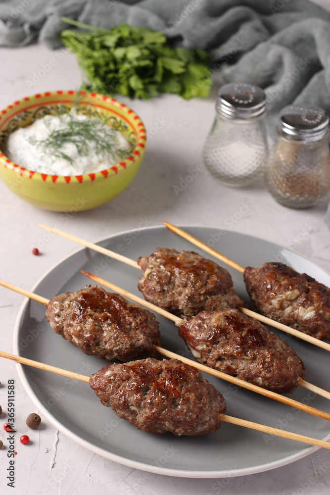 Kofta kebab on wooden skewers on a plate and sauce on the table, traditional dish of Arab cuisine, grilled minced meat shish kebab