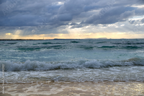 Stormy dark clouds above the sea with sandy beach and curling waves