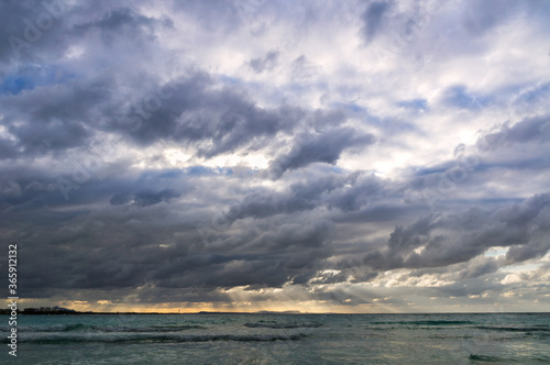 Stormy dark clouds above the sea with sandy beach and curling waves