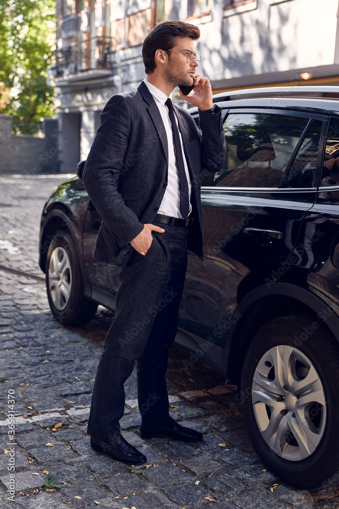 Confident business expert. Full length of handsome young businessman talking on the phone while standing near his car outdoors