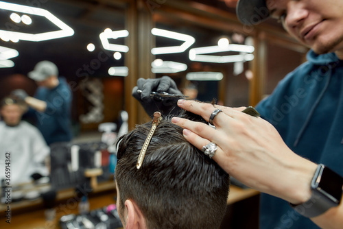 Trendy haircut. Close up shot of professional male barber working with scissors and hair comb, making haircut for client. Man visiting barbershop